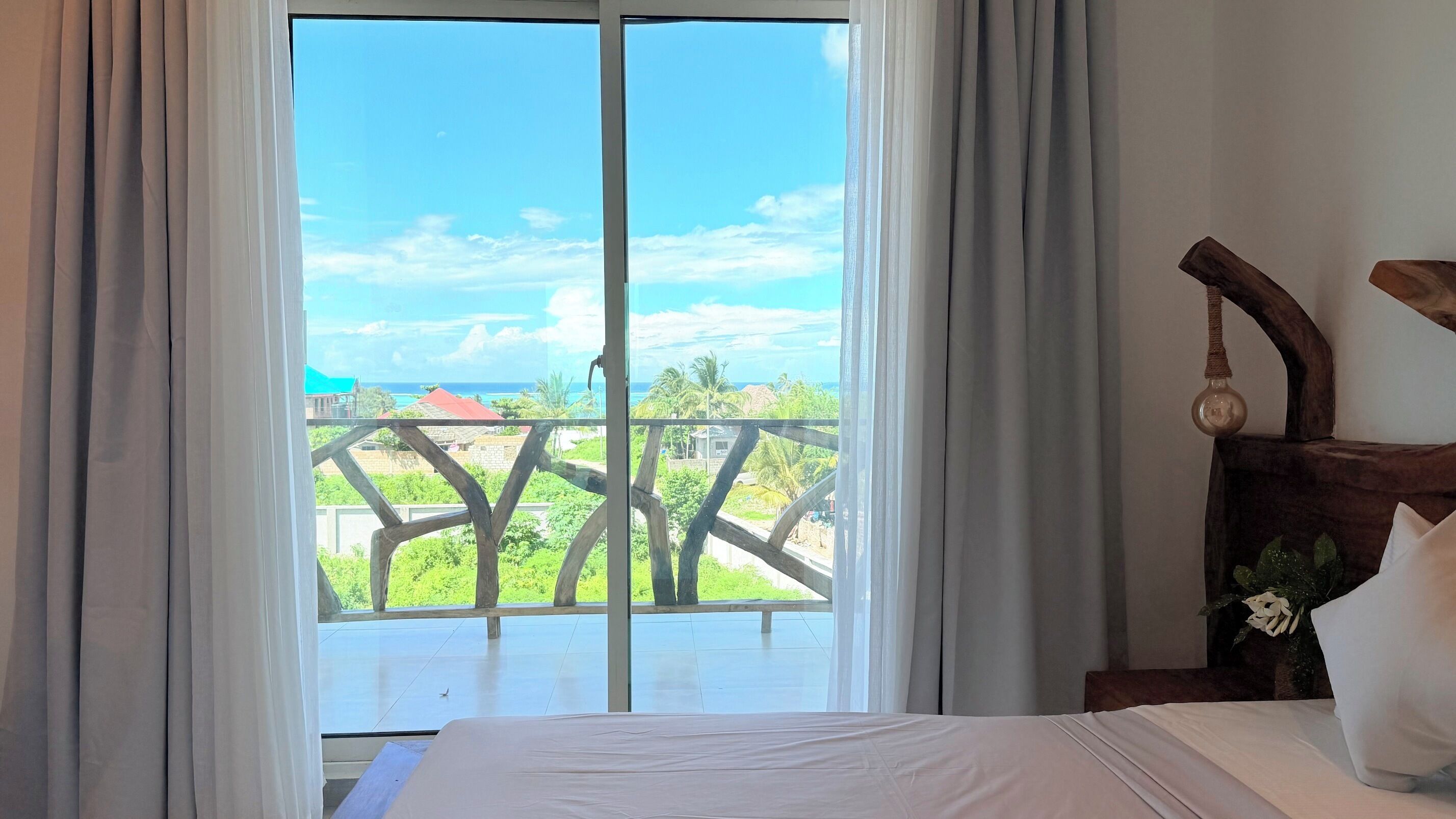 A hotel room with a balcony, a bed, and a view of the ocean and greenery.