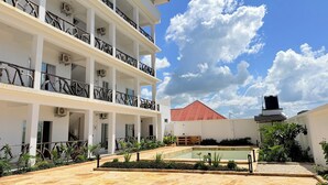 Un immeuble à plusieurs étages doté de balcons, de climatiseurs et d’une cour intérieure avec une piscine et des plantes.