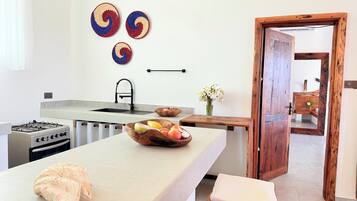 A kitchen with a gas stove, sink, wooden bowl with fruits, and a wooden door.