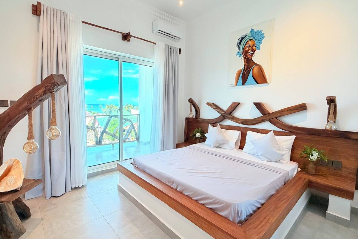 A bedroom with a large bed, wooden headboard, a view of the ocean, and a unique wooden sculpture.