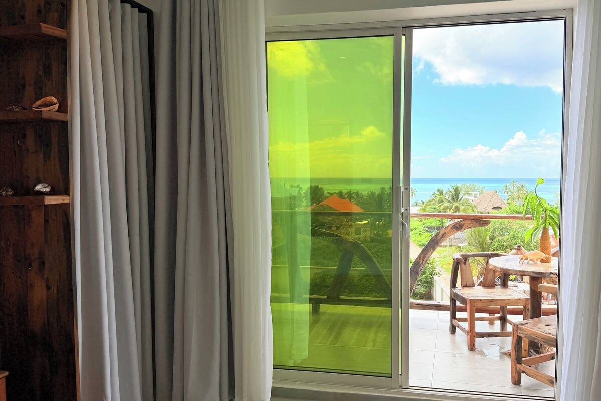 A balcony with a view of the ocean, wooden furniture, and a sliding glass door.