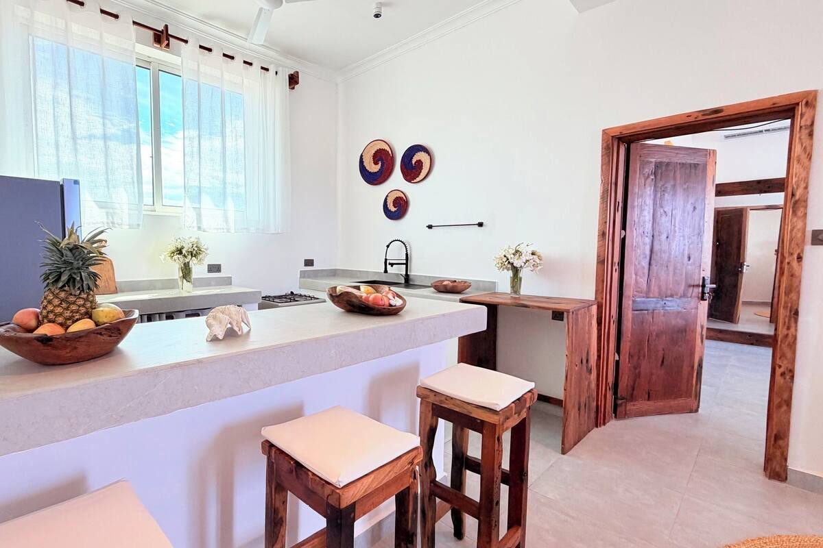 A modern kitchen with a central island, bar stools, a large window, and decorative wall art.