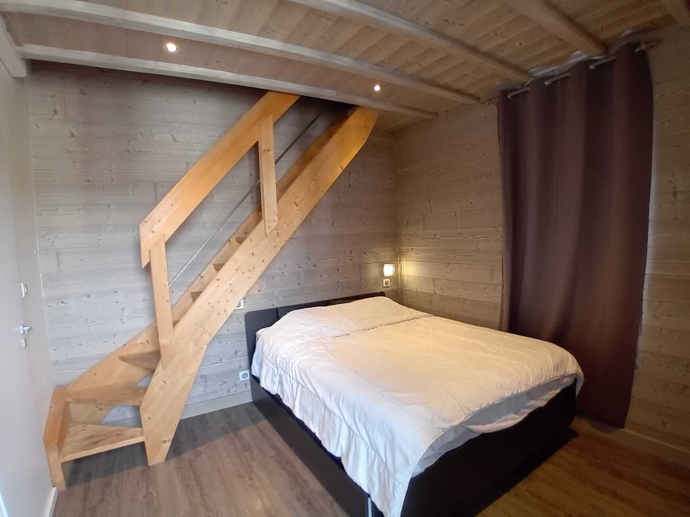 A bedroom with a wooden staircase, a bed, and a wall-mounted light fixture.