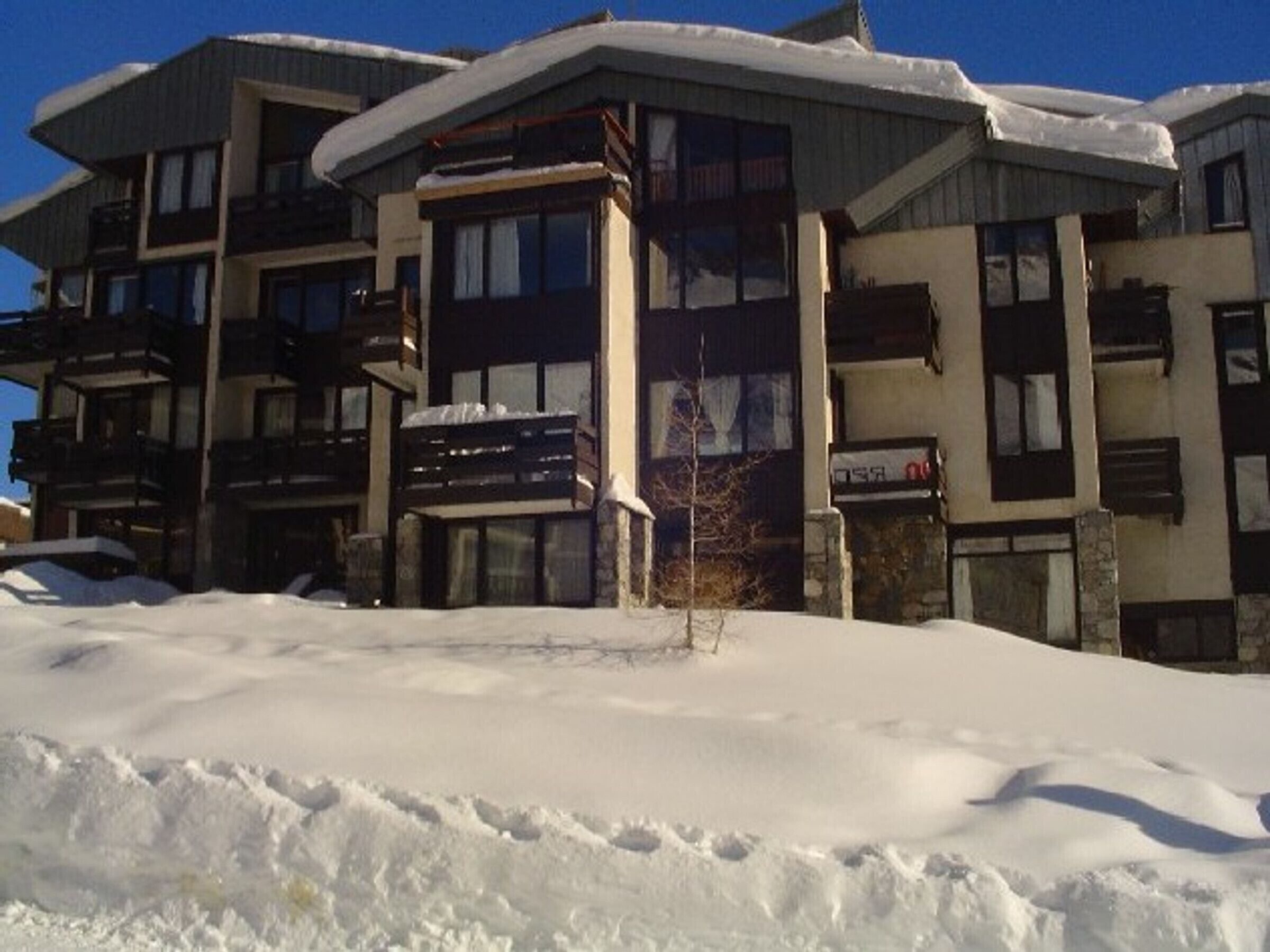 Ett hotell med flera våningar, balkonger, en fasad av sten och en omgivning täckt av snö.