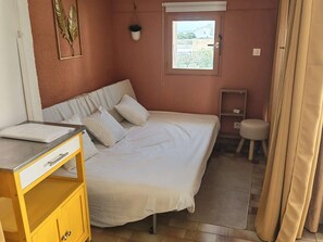 A bedroom with a bed, a bedside table, a small stool, a window, and a potted plant. - Studio cabin, pets allowed - Mountain view (Le Barcarès)