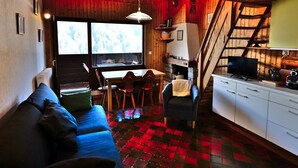 A cozy cabin interior with a sofa, dining table, chairs, a fireplace, and a kitchen area. - Studio with mezzanine near village center - 4 guests (Le Grand-Bornand)