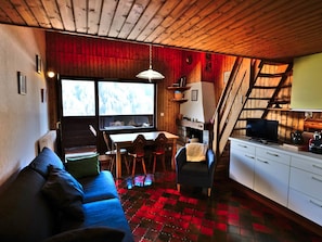 Un interior de cabaña acogedor, con sofá, mesa de comedor, sillas, chimenea y zona de cocina.