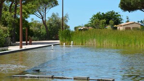 A tranquil outdoor area with a water feature, surrounded by trees and a building in the background. - Apartment with sea view, parking - 4 guests (Six-Fours-les-Plages)