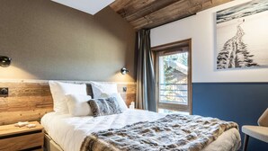 Ein Schlafzimmer mit einem Holzkopfteil, einem großen Bett mit weißer Bettwäsche, einem Fellüberwurf, einem Nachttisch und einem gerahmten Bild an der Wand.