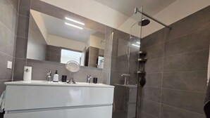 Une salle de bain moderne avec une douche à parois de verre, un grand miroir et un meuble-lavabo blanc.
