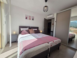 A bedroom with a bed, bedside tables, a hanging light fixture, and a view through an open door. - Apartment, AC, parking - 4 guests (Lumio)