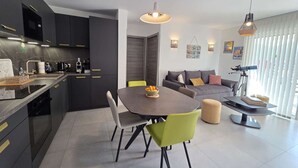 Une cuisine moderne avec des meubles de couleur sombre, un coin repas avec une table ronde et des chaises, et un salon avec un canapé et un télescope.