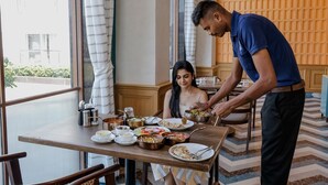 A dining area with a table set for two, various dishes, and a waiter serving food. - Estrella The Resort (Karjat)