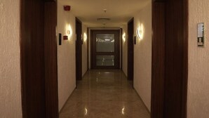 A hotel hallway with wooden doors, wall-mounted light fixtures, and a ceiling vent. - Estrella The Resort (Karjat)