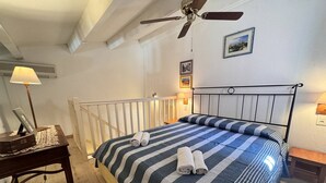 Een slaapkamer met een bed, een bureau, een lamp, een plafondventilator en een foto aan de muur.