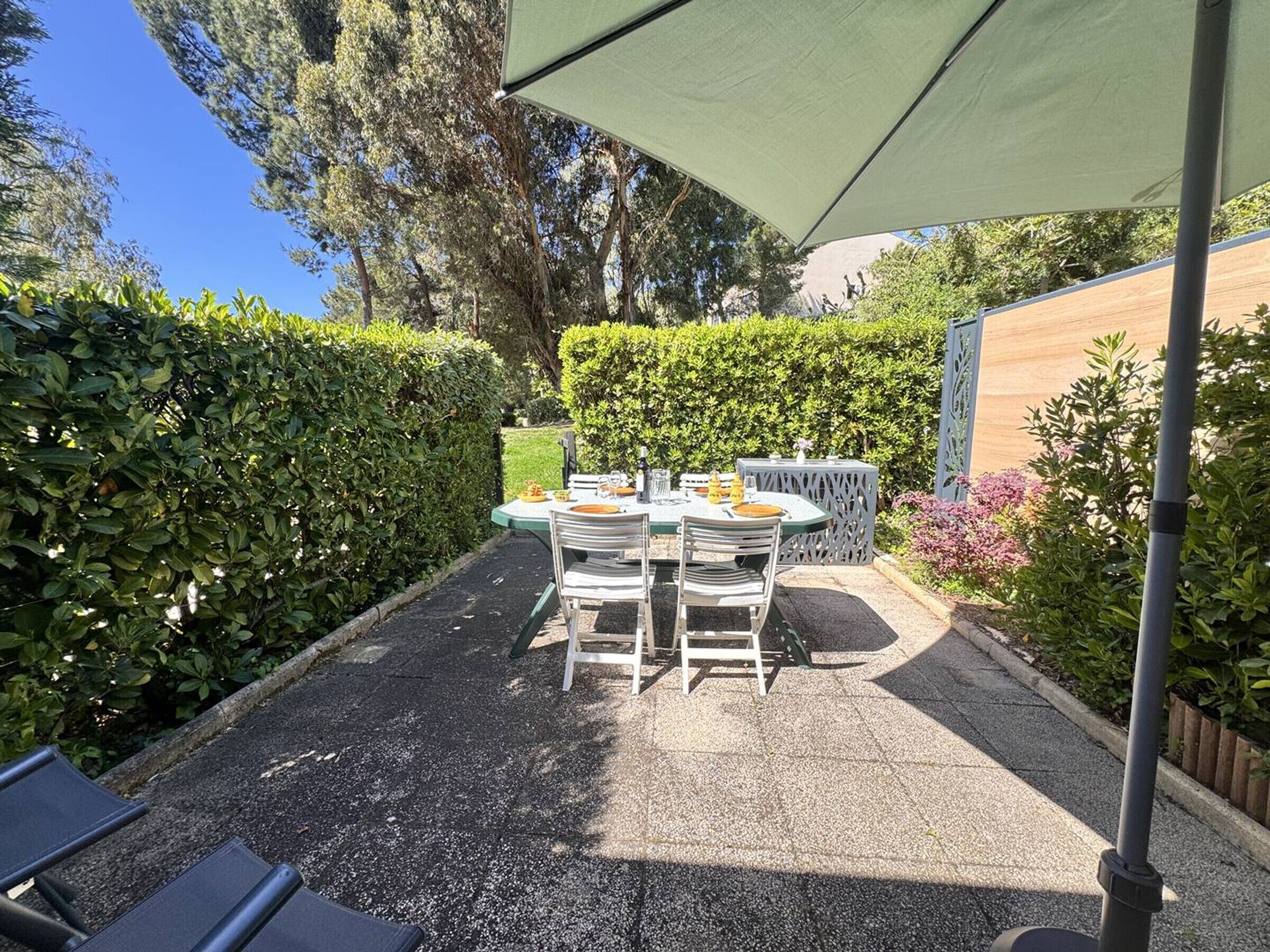 A patio with a table and chairs, surrounded by hedges and trees.