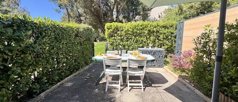 A patio with a table and chairs, surrounded by hedges and trees.