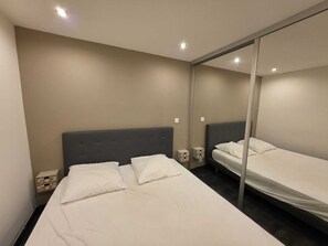 Una habitación con una cama grande, una cama más pequeña, un espejo y una mesita de noche.