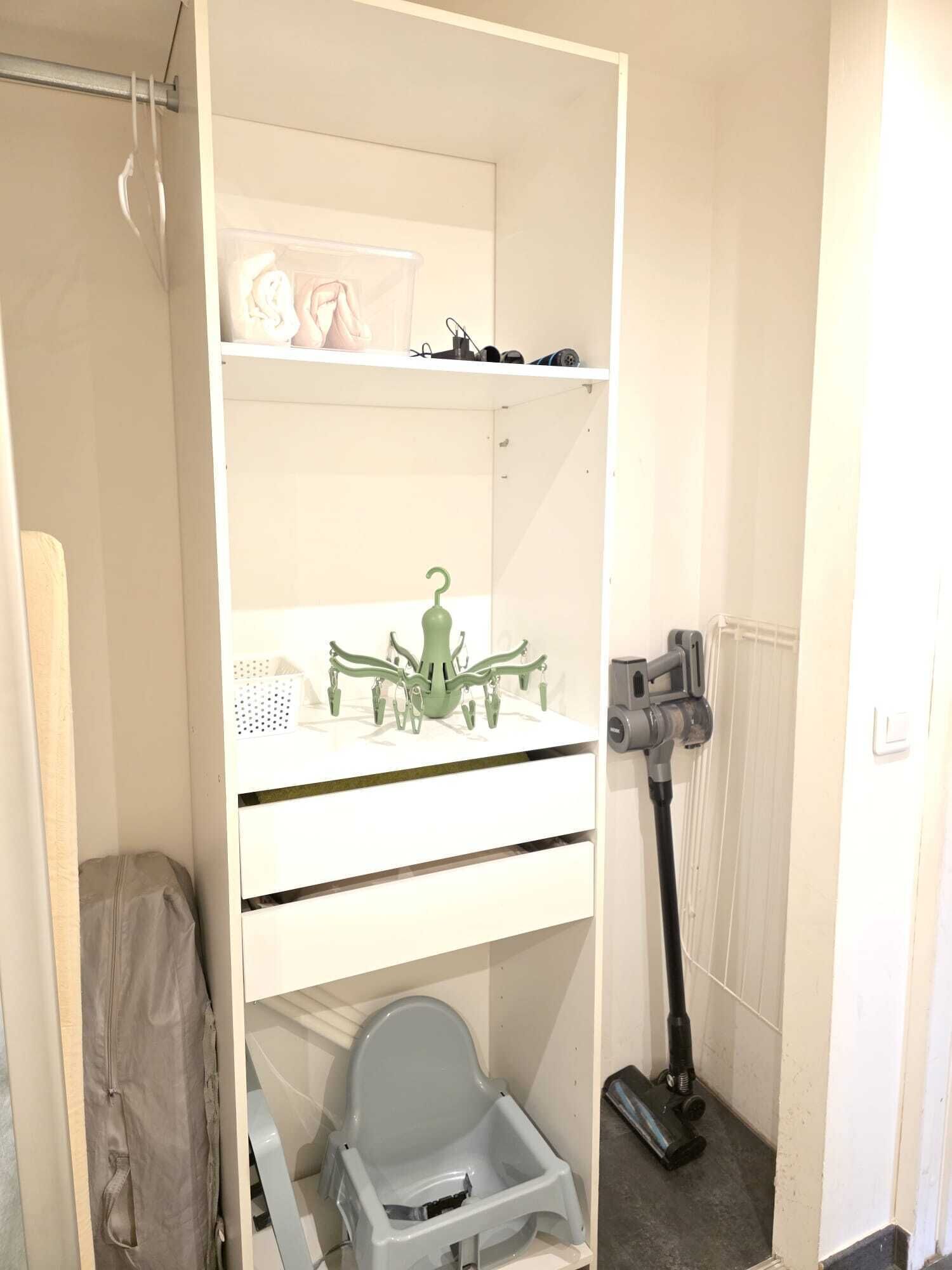 A white room with a shelf, a green object, a gray chair, and a vacuum cleaner.