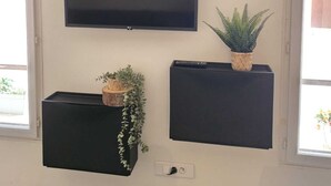 A wall-mounted clock, a flat-screen TV, and two black cabinets with plants.