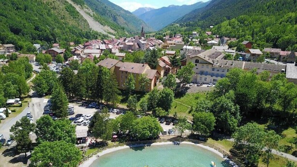 A mountainous town with a central square, buildings with red roofs, and a clear blue lake.