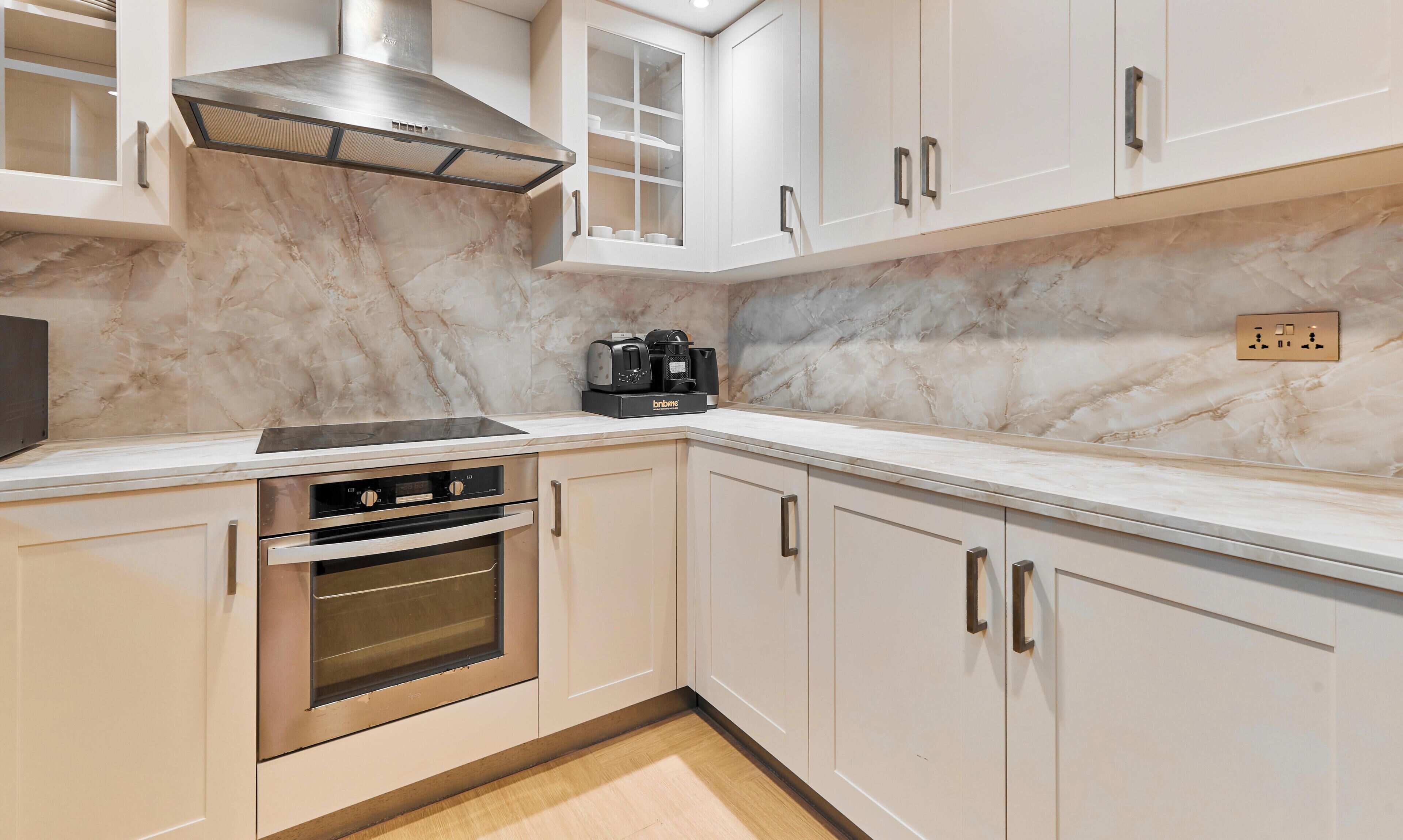 A kitchen with white cabinets, a stainless steel range hood, a built-in oven, and a coffee maker on the countertop.