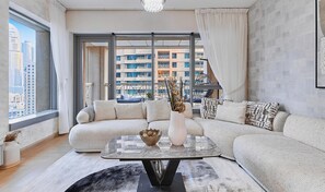Ein modernes Wohnzimmer mit einem Ecksofa, einem Glastisch und Blick auf eine Skyline durch große Fenster.