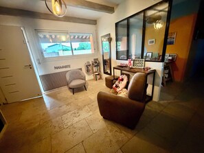 A living room with a large window, a sofa, a chair, a small table with a teddy bear, and a wall with a mirror and framed pictures. - Comfortable air-conditioned house in the heart of Provence (L'Isle-sur-la-Sorgue)