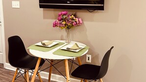 A dining area with a TV mounted on the wall, a round table with green placemats, two black chairs, and a vase with pink flowers. - Dragonfly Inn II 
Fabulous 2BR 1BA modern downtown apt  walk to everything (Winchester)