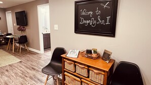 A reception area with a welcome sign, a television, wicker baskets, and black chairs. - Dragonfly Inn II 
Fabulous 2BR 1BA modern downtown apt  walk to everything (Winchester)