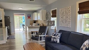 A spacious living area with a sofa, a wooden coffee table, and a dining area with a chair and table. - Charming Cottage with Pool. Close to shops, restaurants and farms (West Cape May)