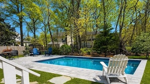 A rectangular swimming pool with a stone deck, surrounded by a grassy area and trees. - Charming Cottage with Pool. Close to shops, restaurants and farms (West Cape May)