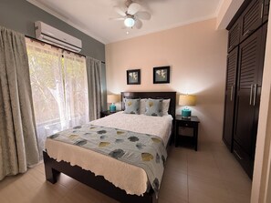 A bedroom with a bed, two bedside lamps, a ceiling fan, and an air conditioning unit. - Tropical 2BR Condo in Playas del Coco – Pool, Walk to Beach & Downtown. (Playas del Coco)