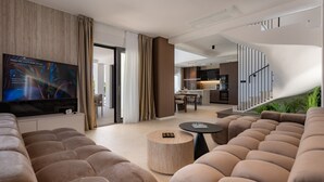 Ein modernes Wohnzimmer mit Flachbildfernseher, einer Couch, einem runden Couchtisch und einer Treppe, die in eine Küche führt.