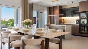 Ein moderner Essbereich mit einem langen Tisch, gedeckt für sechs Personen, einer Vase mit weißen Blumen und einer Küche mit dunklen Holzschränken und einem Edelstahlkühlschrank.