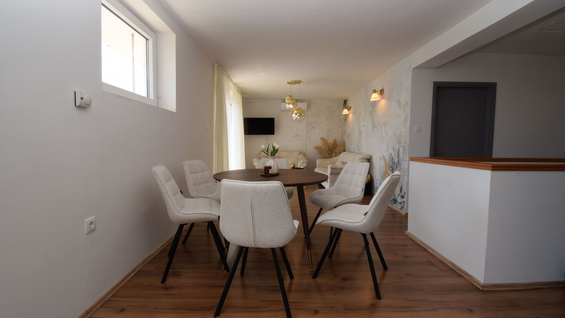 Een eetgedeelte met een ronde tafel en zes stoelen, een flatscreen televisie aan de muur en een raam met een veiligheidsketting.
