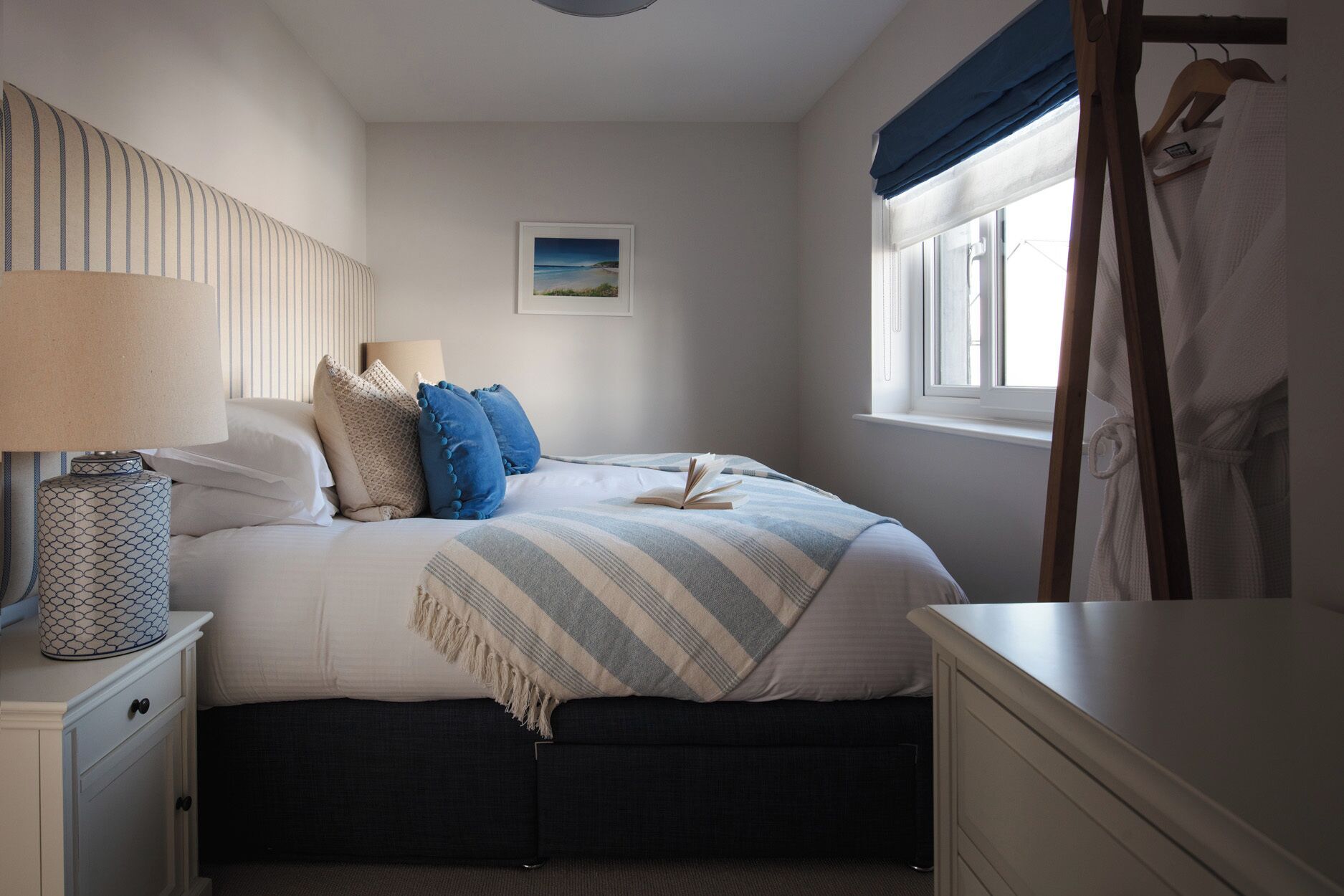 A bedroom with a bed, bedside table, lamp, and a window with curtains.