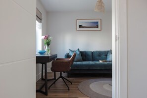 Ein modernes Wohnzimmer mit einem dunkelblauen Sofa, einem braunen Ledersessel, einem kleinen Tisch mit Blumen und einem gerahmten Bild an der Wand.
