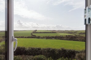 A view through a window with a landscape of rolling green fields and a distant white building. - Polview (Newquay)