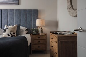 A bedroom with a bed, nightstand, dresser, lamp, and a mirror. - Polview (Newquay)