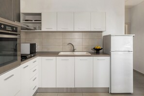 A modern kitchen with white cabinets, a stainless steel oven, a sink, and a refrigerator. - Cozy villa with beautiful large garden (NEA POTIDAIA)