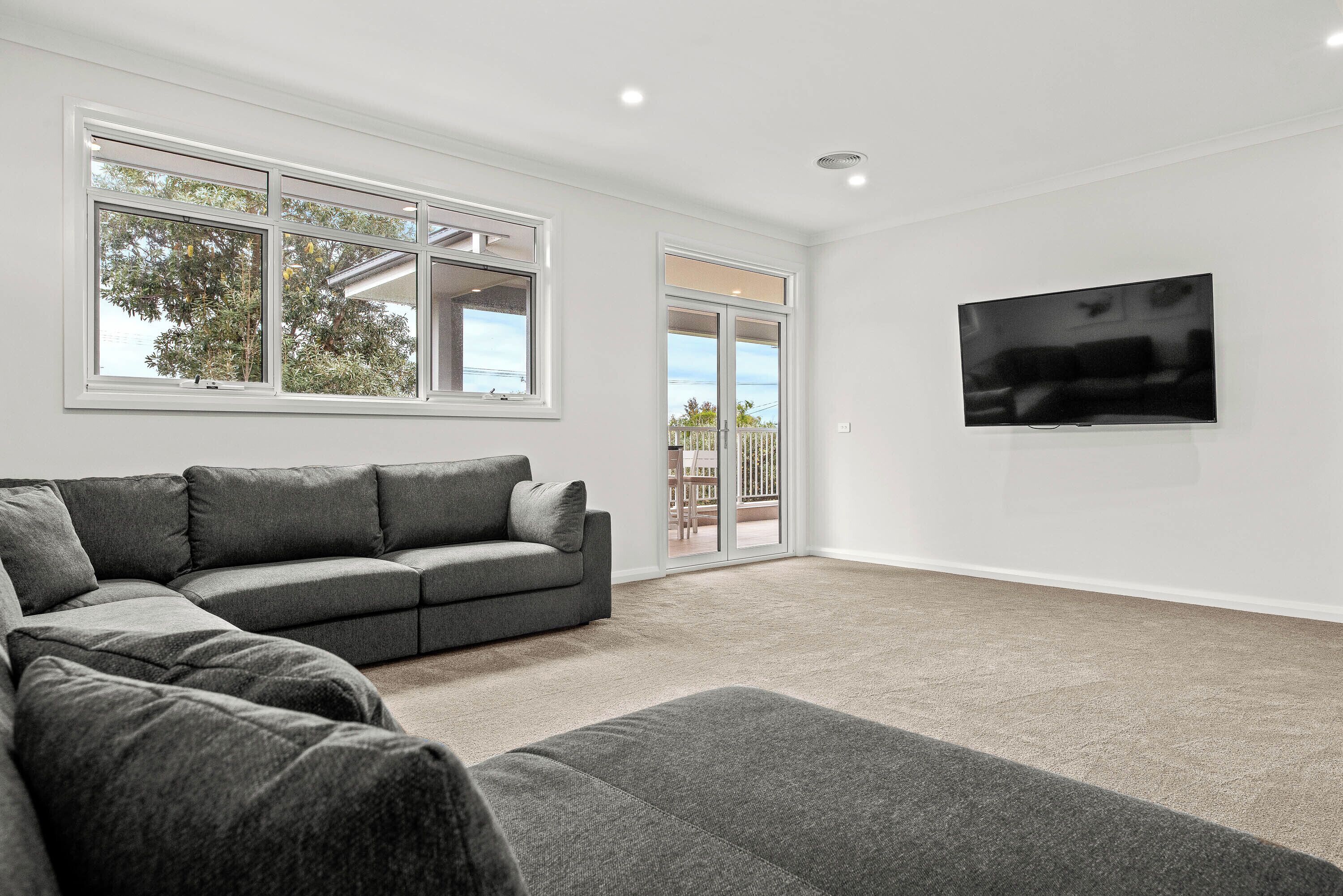 A modern living room with a sectional sofa, a flat-screen TV, and large windows.
