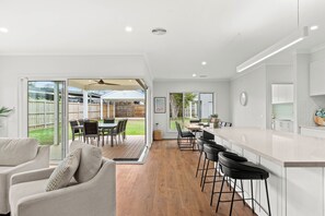 Eine moderne Küche mit Barbereich, Schiebegläsern zu einer Terrasse und einem Essbereich mit Außenmöbeln.