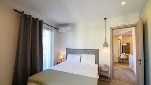 Hotellihuone, jossa on sänky, verhot, ilmastointilaite, yöpöytälamppu ja näkymä viereiseen huoneeseen.