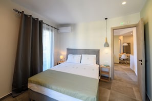 A hotel room with a bed, curtains, an air conditioning unit, a bedside lamp, and a view into the adjacent room. - Sebil domus | Central Stay in Heraklion – Walk Everywhere! (Heraklion)