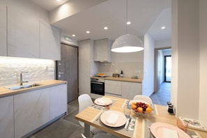 A modern kitchen with a wooden countertop, built-in oven, and a dining area with a table set for two. - Sebil domus | Central Stay in Heraklion – Walk Everywhere! (Heraklion)