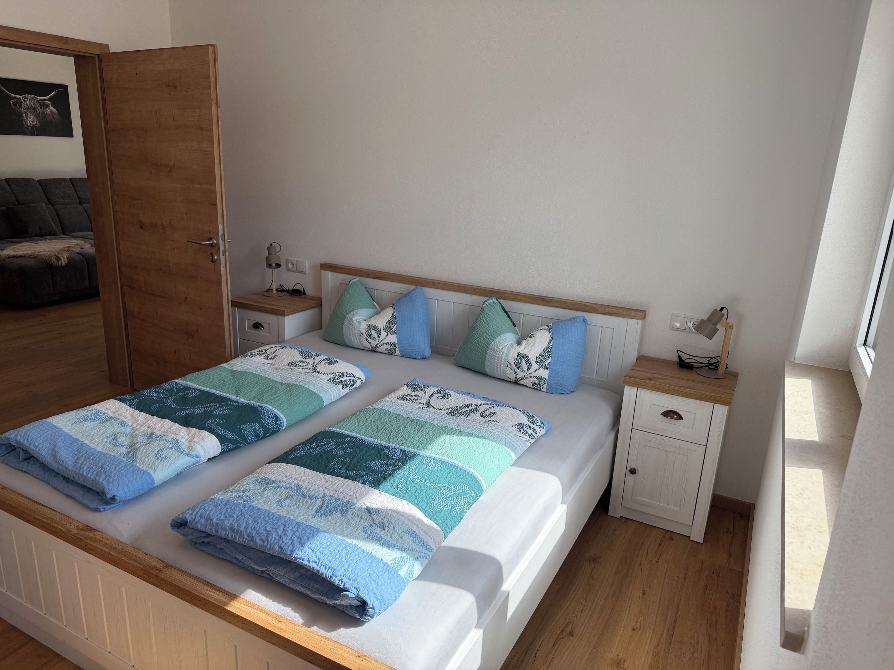 A double bed with a patterned bedspread, two bedside tables with lamps, a nightstand, and a wooden headboard.