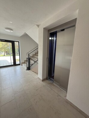 Ein geräumiger Flur mit einem modernen Aufzug und einer Treppe, die zu einem Außenbereich führt.