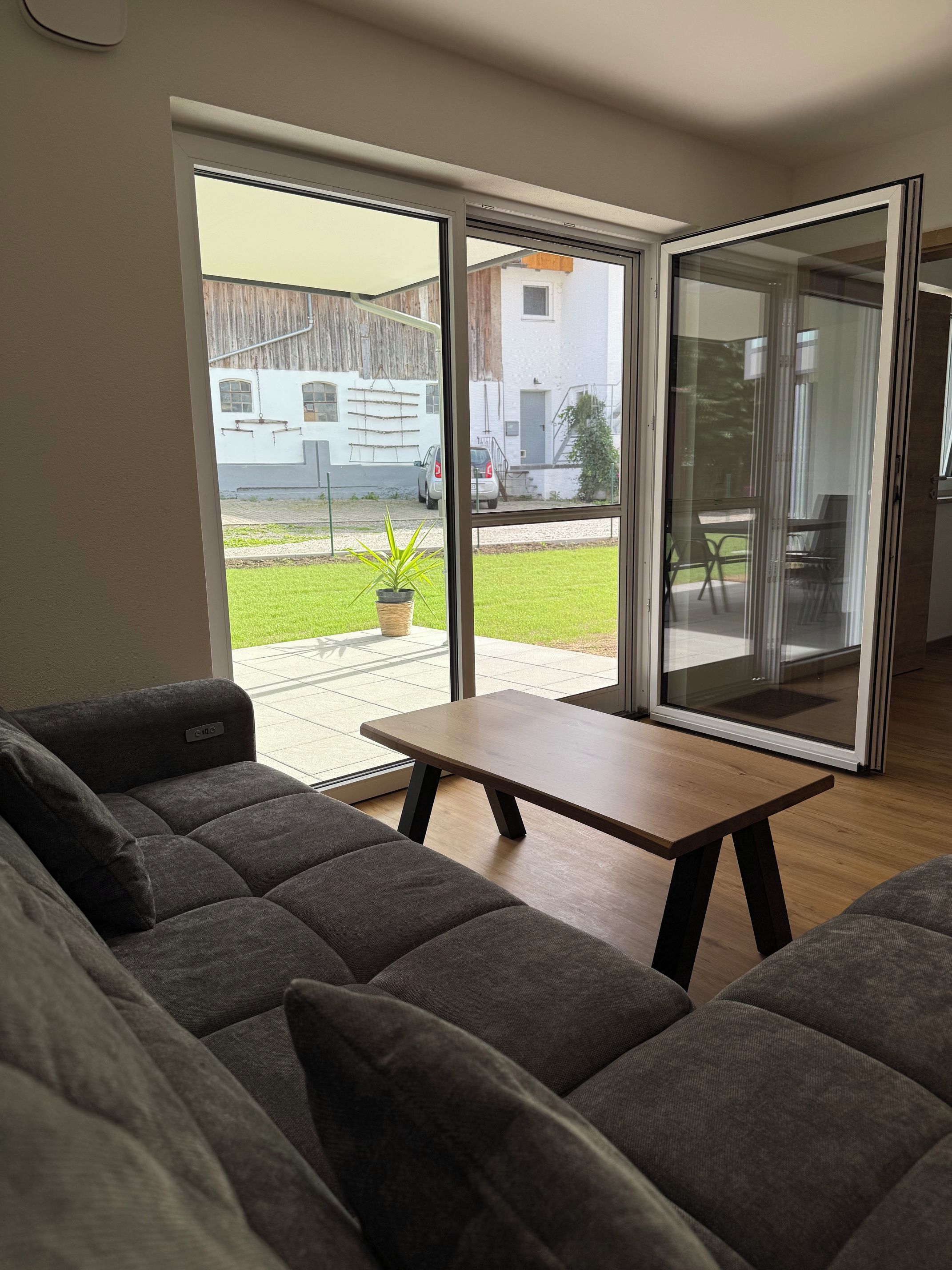 A modern living room with a sofa, a small table, and a sliding glass door leading to an outdoor area.