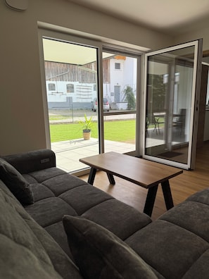 Una sala de estar moderna con un sofá, una mesita y un ventanal corredera que da a un espacio exterior.